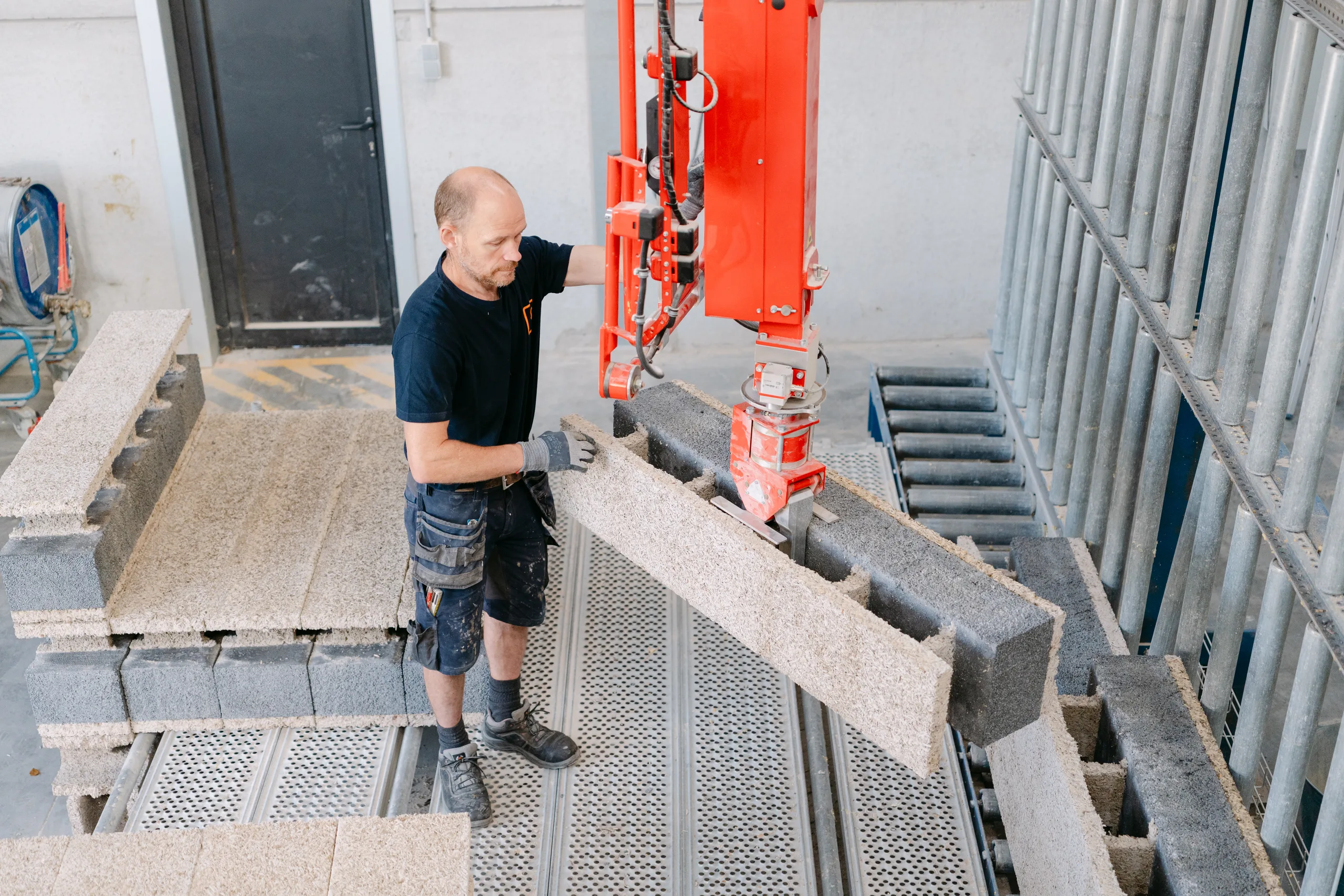 Man positioneert betonnen blokken op een bouwwerf met een rode hefmachine