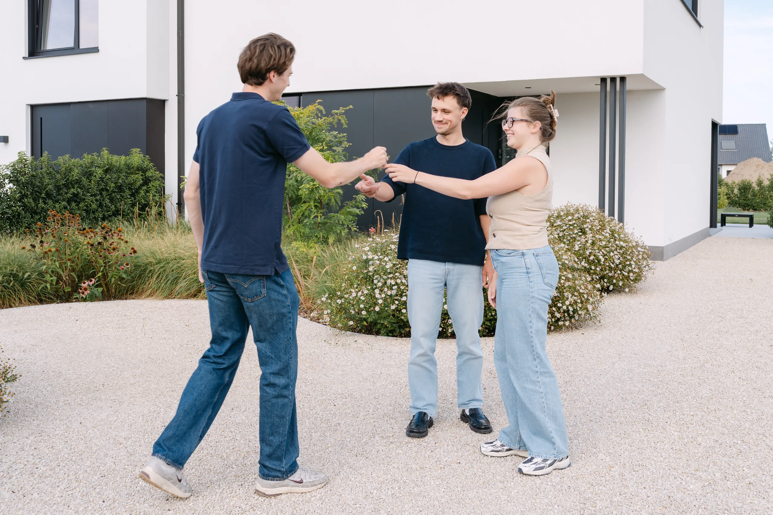 Drie personen geven elkaar een hand voor een moderne woning met witte gevel en donkere deuren