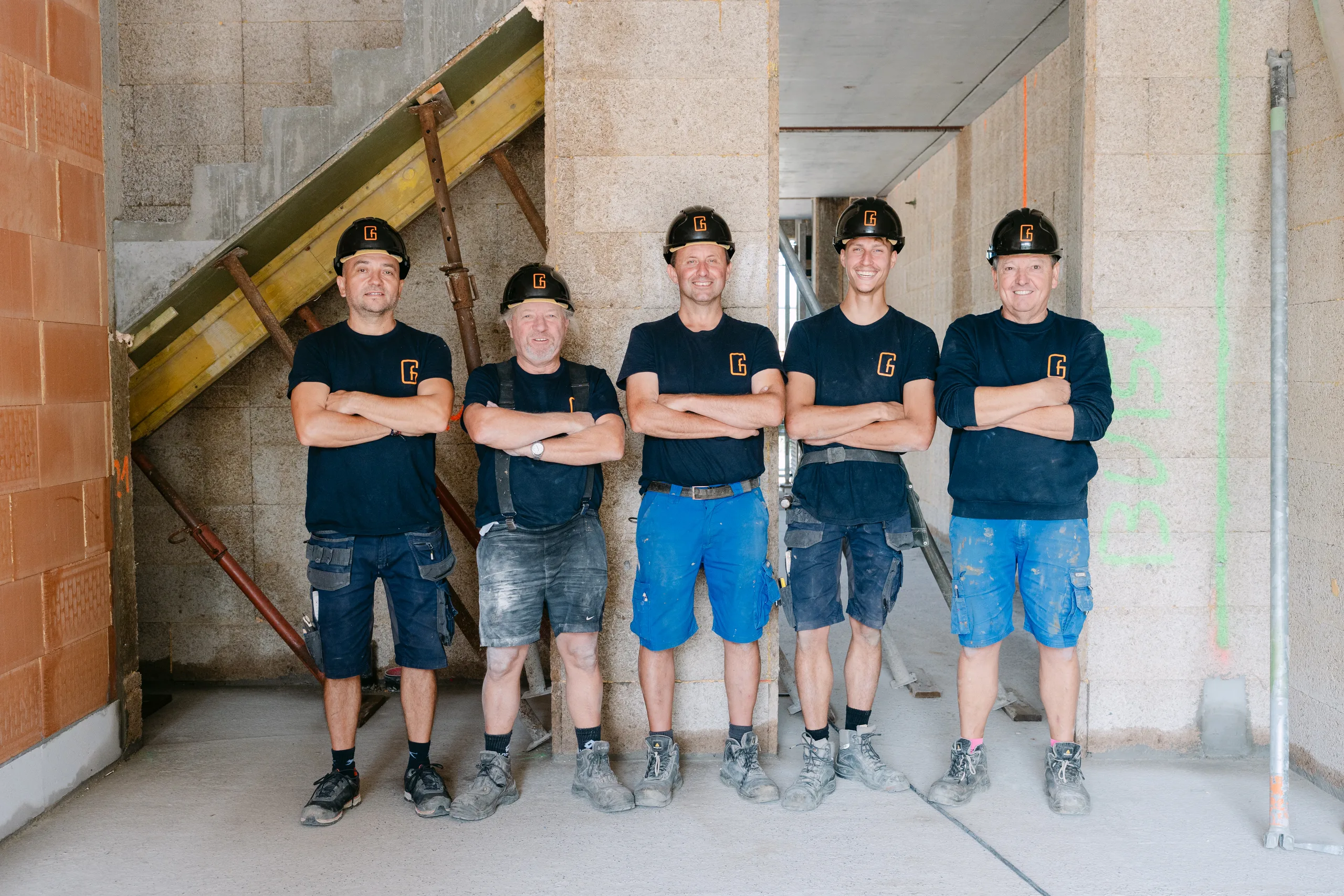 Vijf bouwvakkers in teamshirts poseren op een bouwwerf in aanbouw