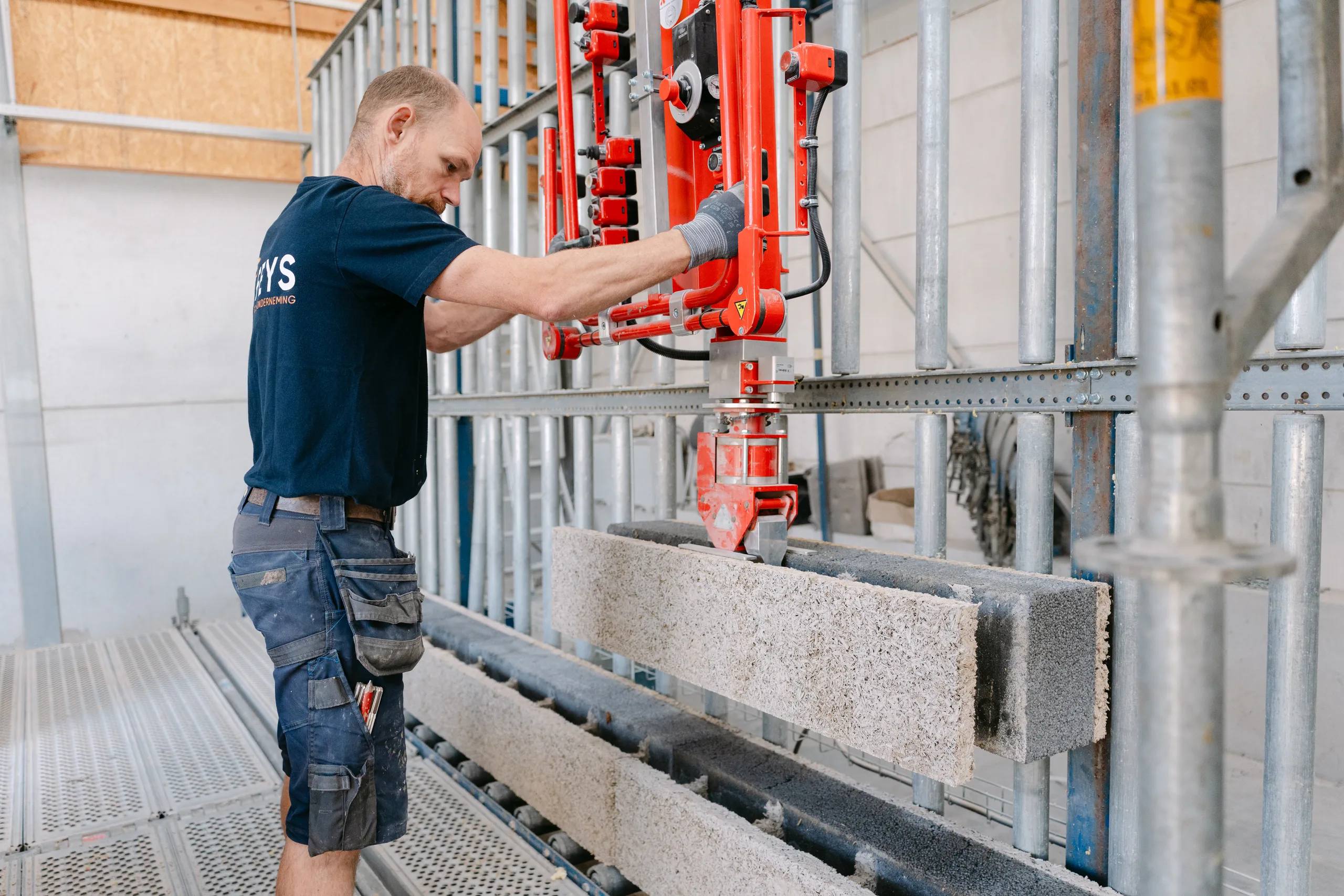 Arbeider bedient rode hefmechanisme op bouwwerf met betonblokken en stalen constructie