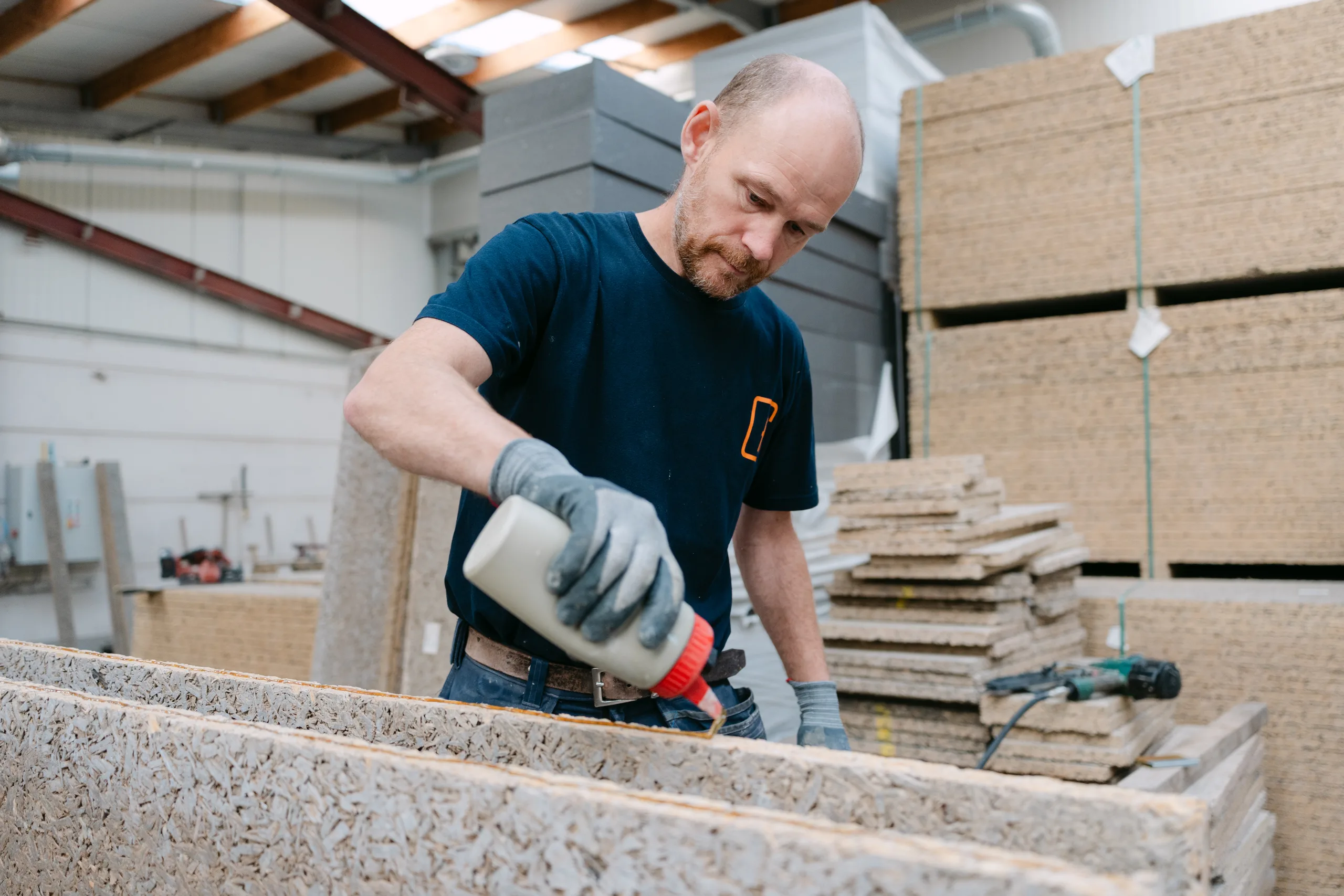 Arbeider bewerkt materiaal in een werkplaats met stapels bouwmaterialen op de achtergrond