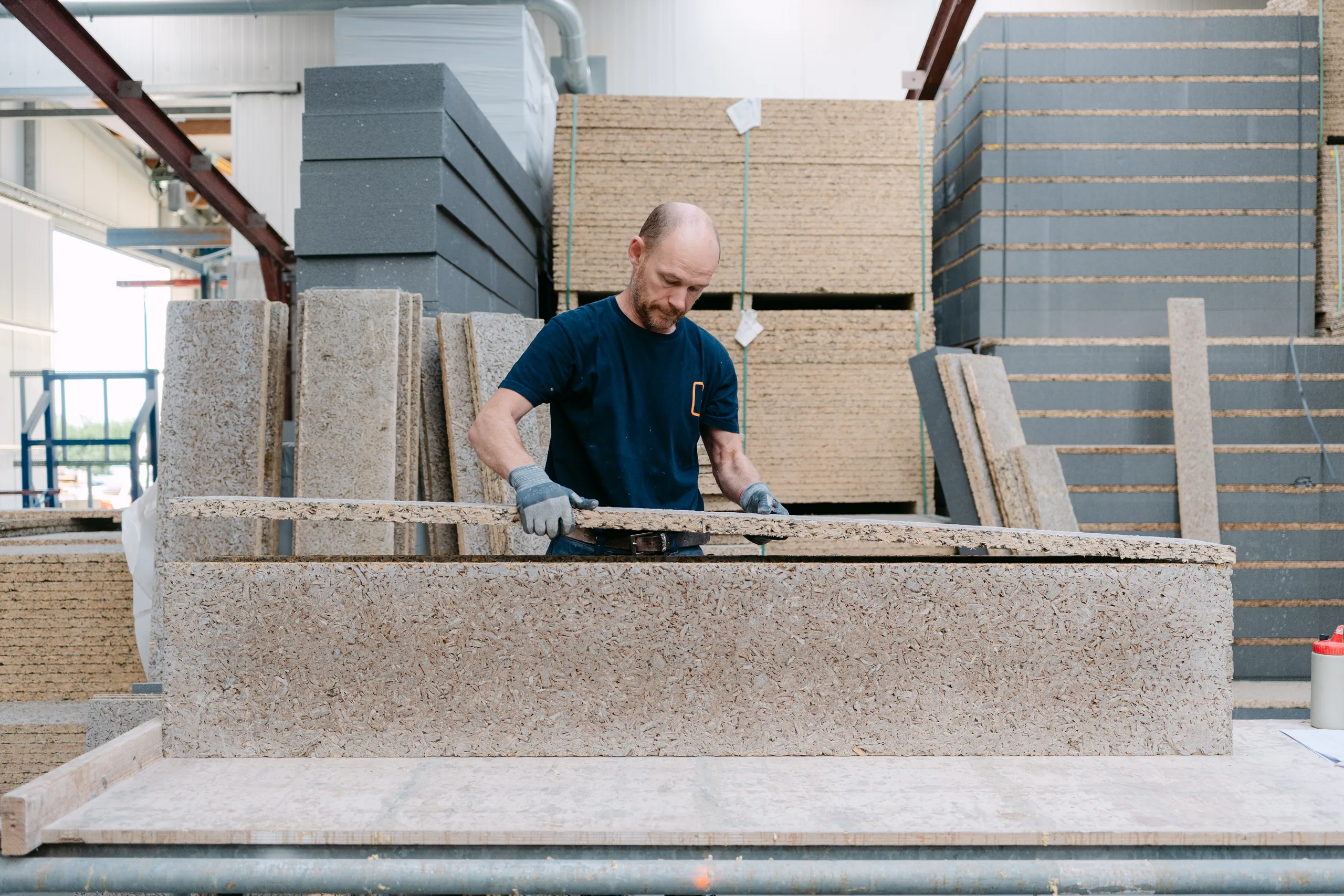 Werker bewerkt betonnen element op een bouwwerf met stapels materialen op de achtergrond