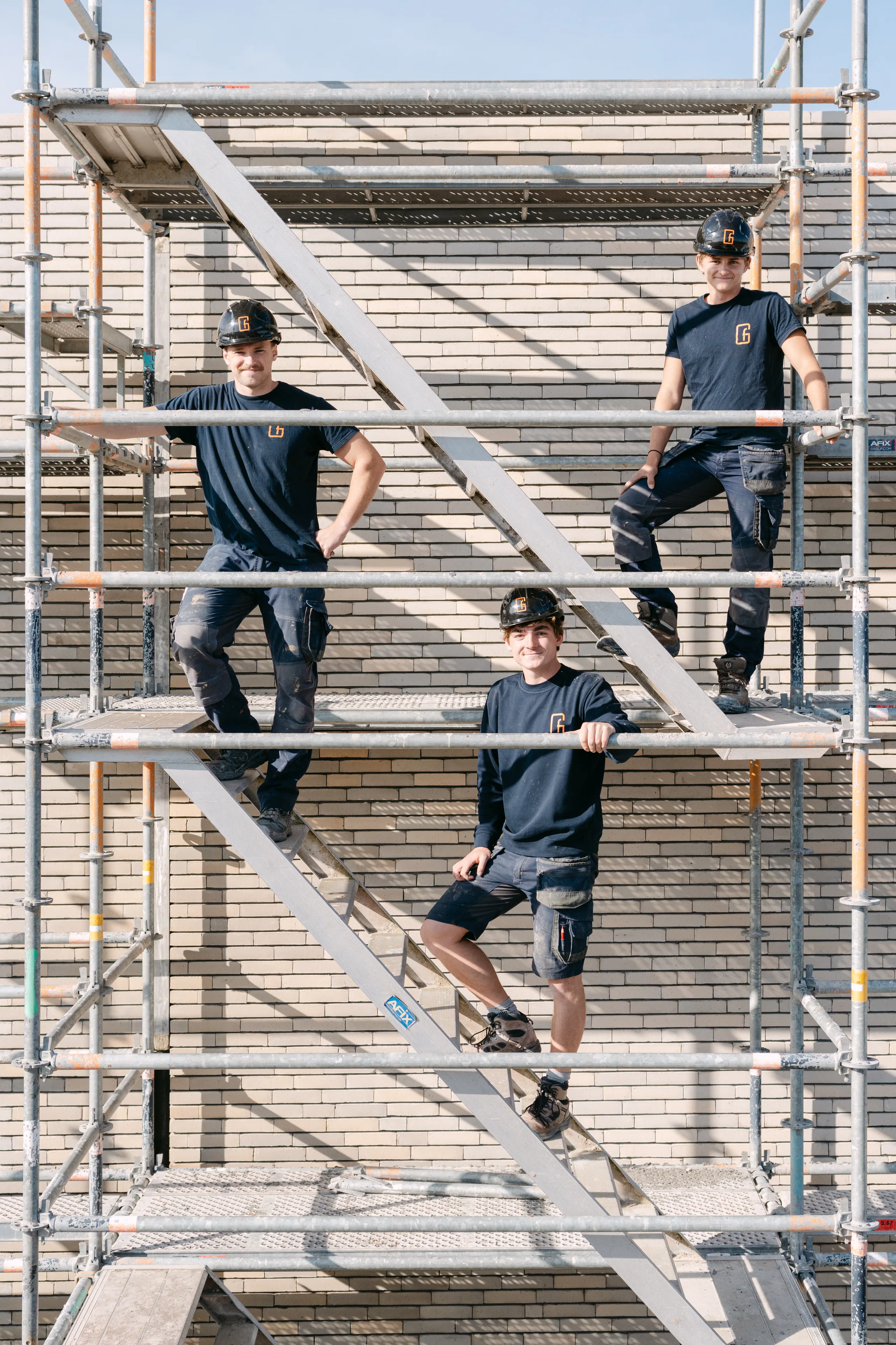 Drie bouwvakkers poseren op een steiger voor een bakstenen gevel in aanbouw