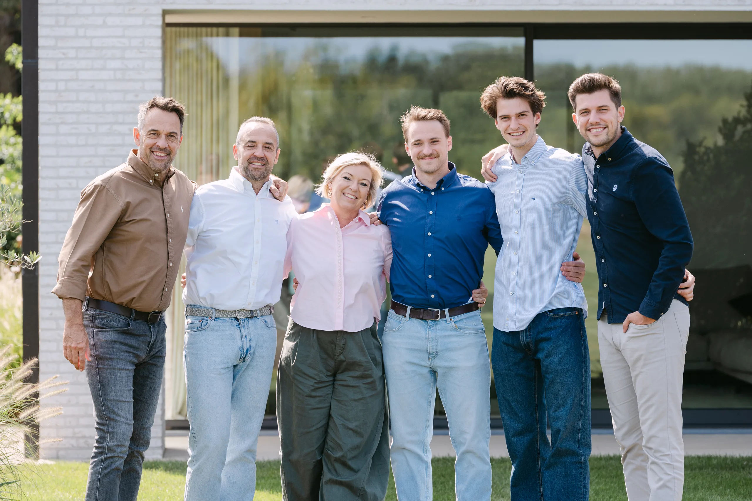 Zes personen poseren voor een groepsfoto voor een modern wit huis met grote ramen