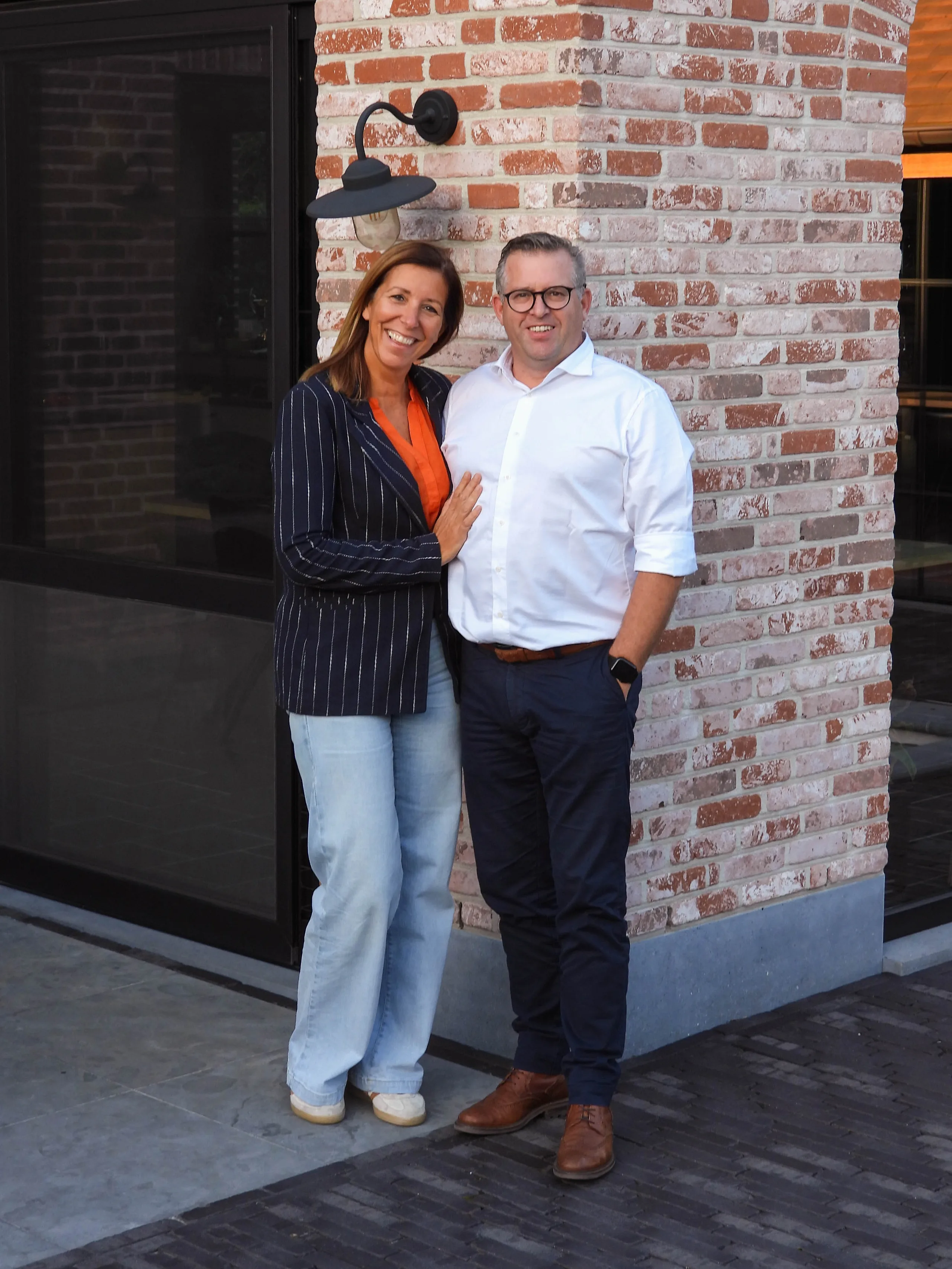 Twee personen poseren voor een bakstenen gevel met zwarte lamp