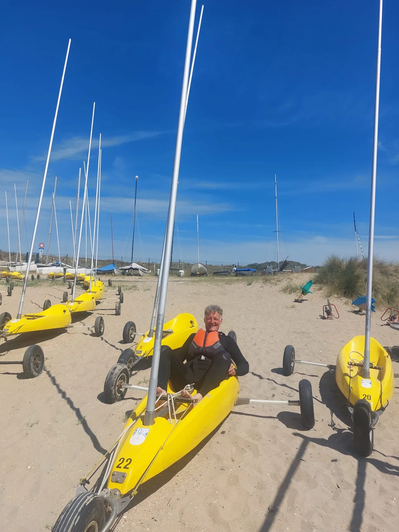 Rij gele zeilboten op het strand met een man in wetsuit op het zand