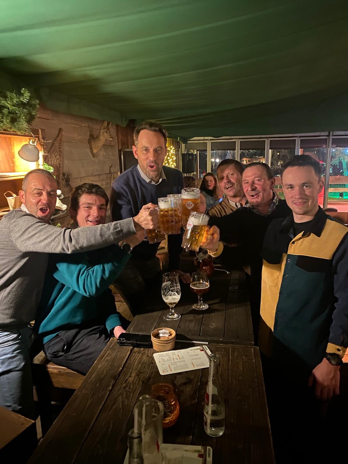 Groep mannen proosten met bierglazen in een ingerichte ruimte met grote ramen