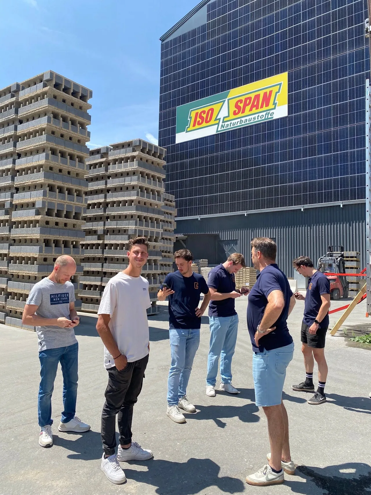 Groep mensen op een bouwwerf met betonnen woningblok en isolatiematerialen op de achtergrond