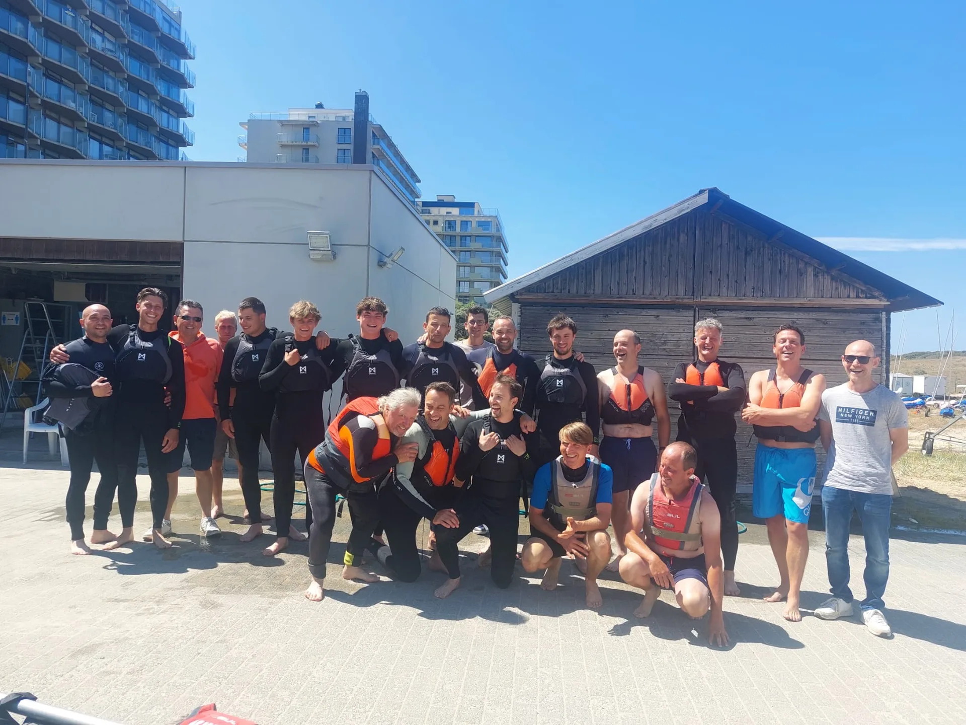 Groep mensen in zwem- en sportkleding poseert voor een beachclub aan het water