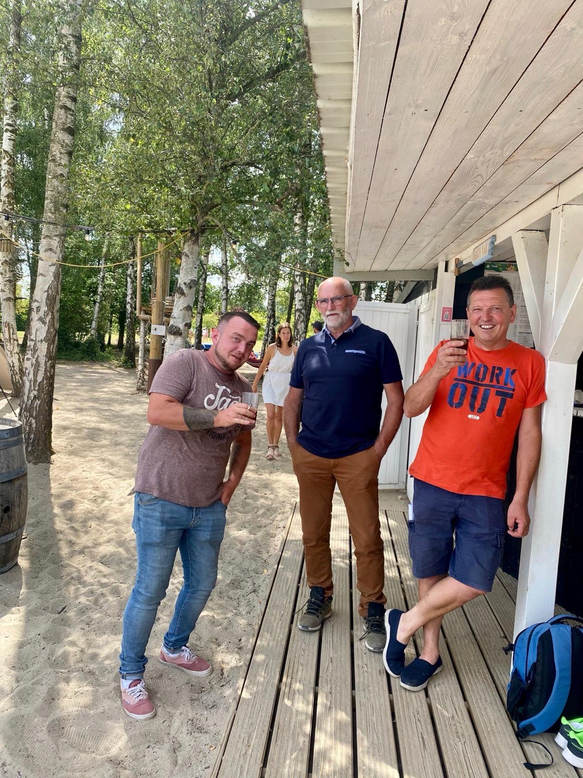 Groep mensen op een houten terras onder een luifel tussen berkenbomen, genieten van een moment samen