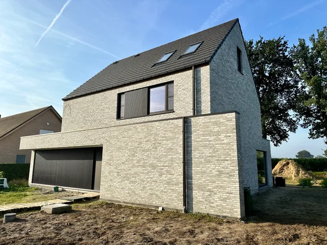 Nieuwbouwwoning met gele gevelsteen, antraciet dak en grote raampartijen op een bouwterrein