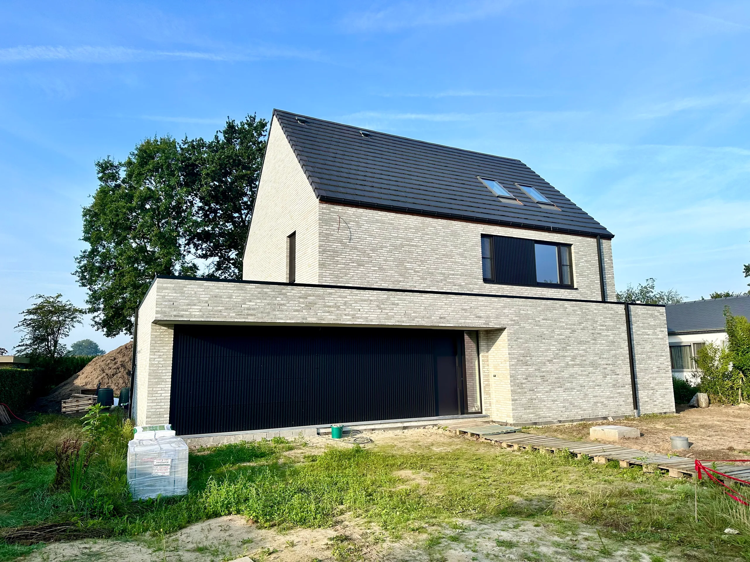 Nieuwbouw woning met gevelsteen in aanbouw, grote garaageopening en donkere dakpannen
