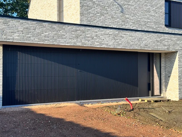 Voorgevel van moderne woning met gevelsteen en grote lamellendeur aan oprit