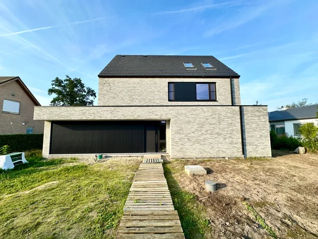 Moderne woning met bakstenen gevel, grote raampartijen en houten looppad naar voordeur