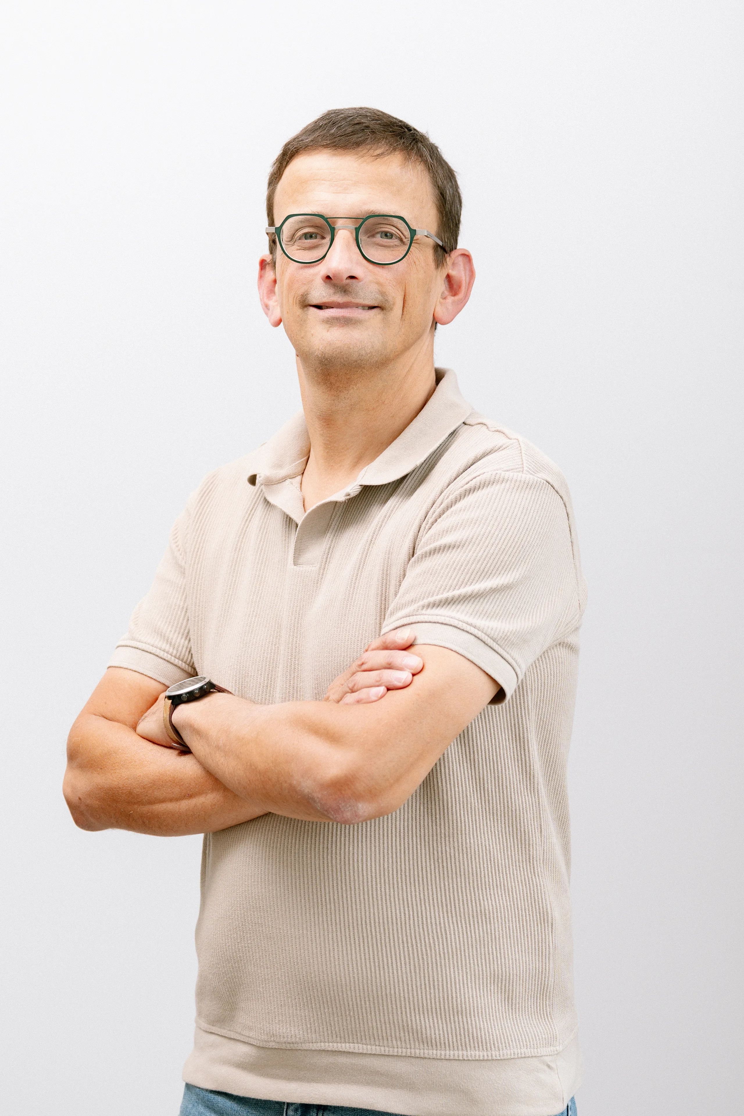 Portretfoto van een man met bril en gekruiste armen tegen een witte achtergrond
