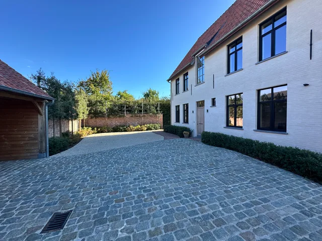 Moderne woning met witte gevel en grote raampartijen, aangesloten oprit met klinkers
