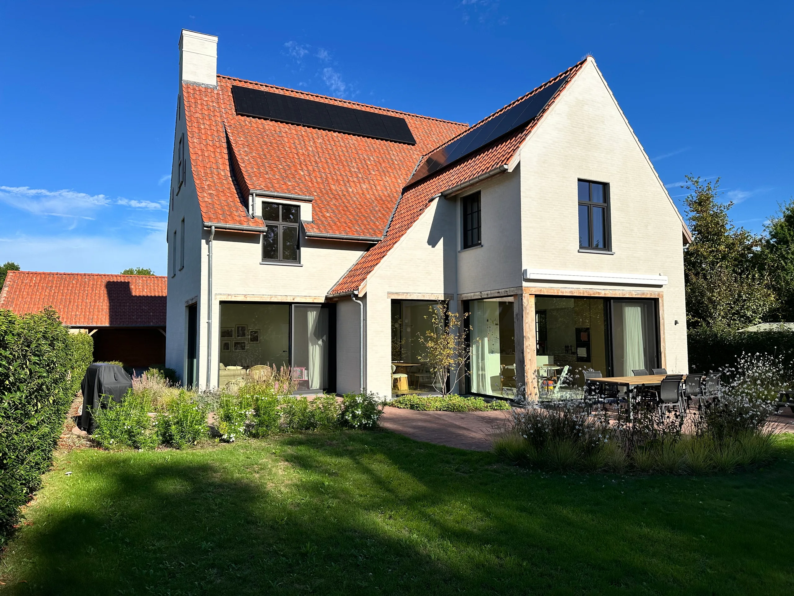 Moderne woning met witte gevel, grote raampartijen en oranje dakpannen, gezien vanaf de tuin