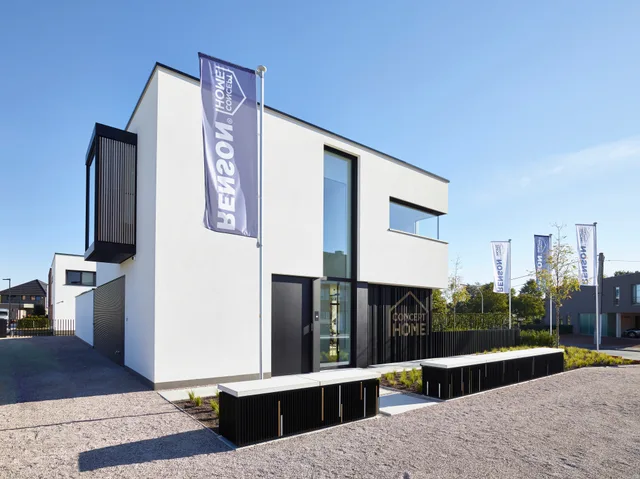 Moderne woning met witte crepi, grote raampartijen en zwarte stalen details op het bouwterrein