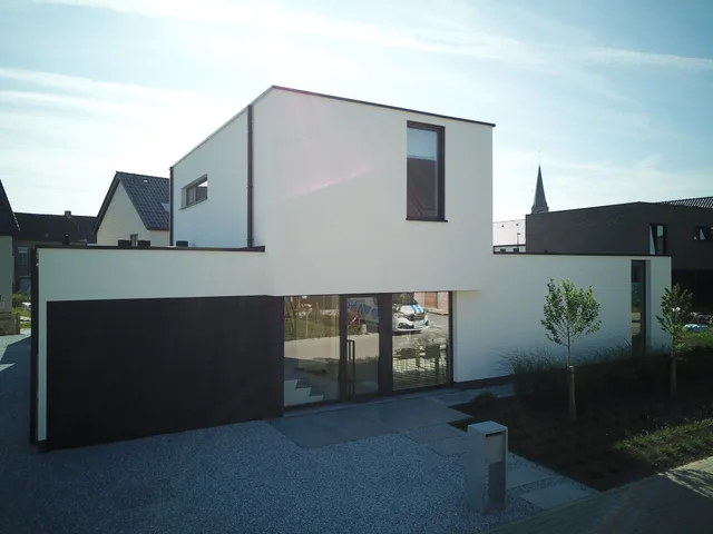 Modern afgewerkt woonhuis met witte gevel, zwarte garage en grote raampartijen aan de voorzijde