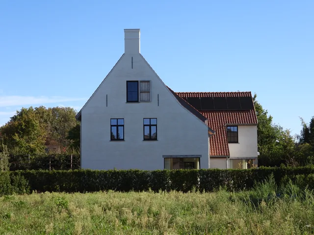 Moderne woning met witte gevel en traditionele dakkapel met rode pannen, omgeven door groen