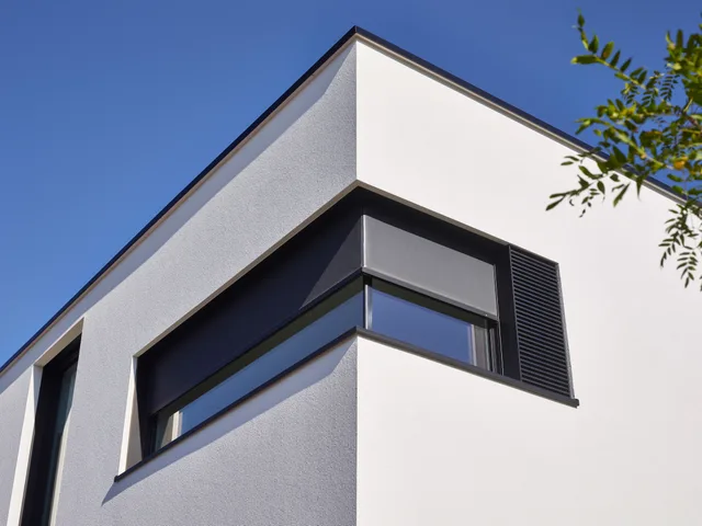Hoekdetail van moderne woning met witte crepi gevel en zwarte aluminium raamkozijnen met lamellen