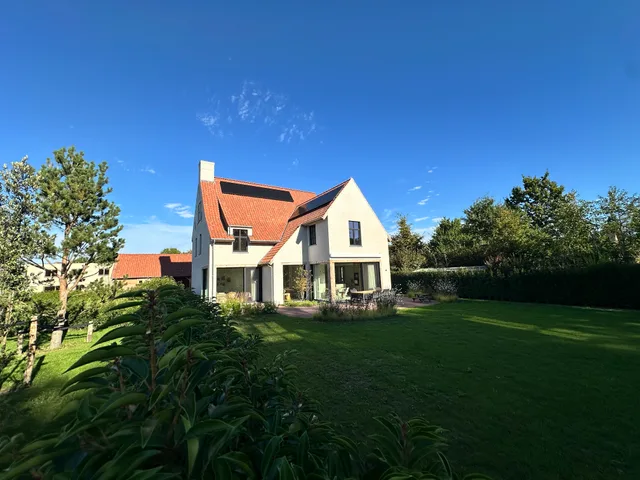 Moderne woning met witte gevel, oranje dakpannen en dakkapel, omgeven door groene tuin