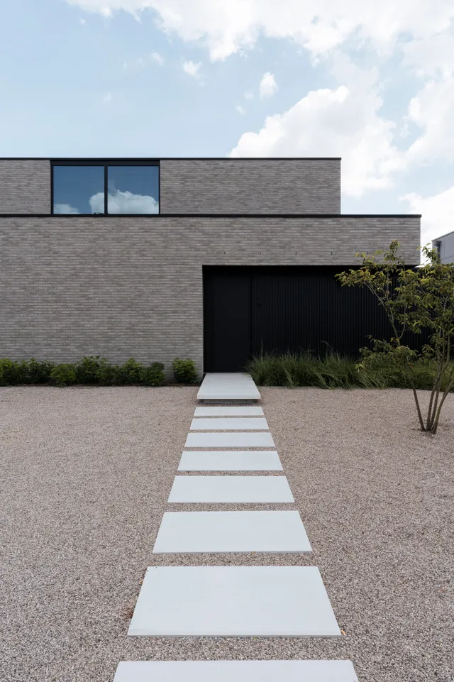 Moderne woning met grijze baksteengevel, grote raampartijen en toegangspad naar de ingang