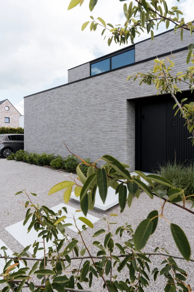 Moderne grijze gevelbekleding met grote raampartijen en zwarte deur