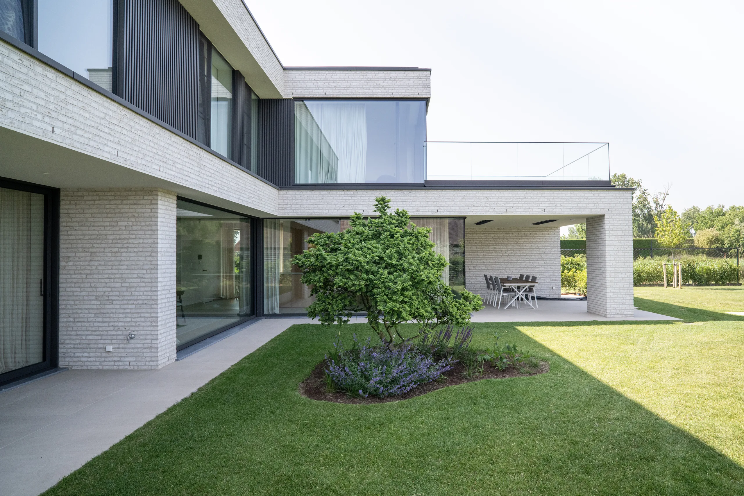Moderne woning met witte gevelsteen, grote raampartijen en overkapte terras aan de tuin