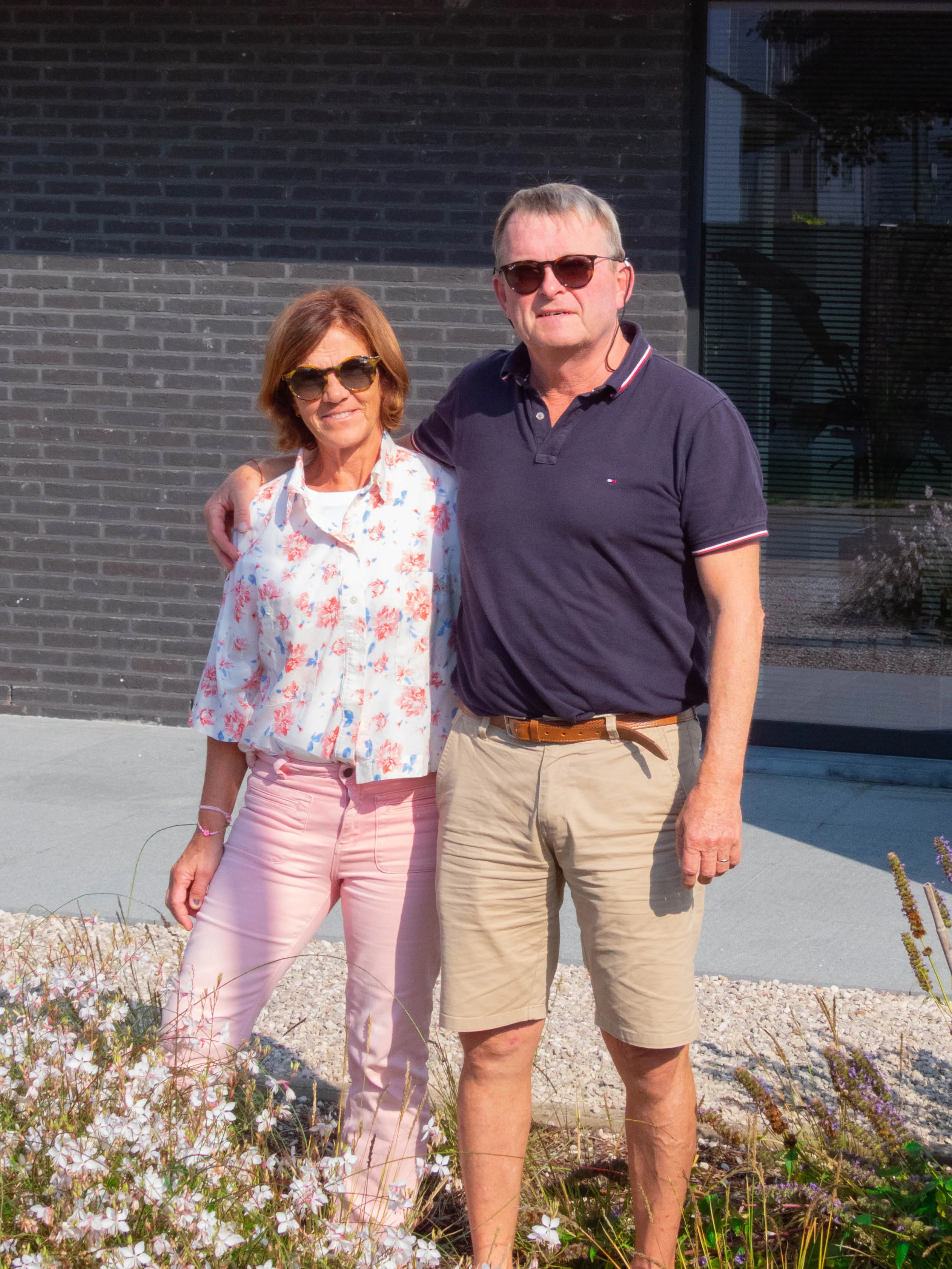Twee personen poseren in een moderne tuin voor een bakstenen woning